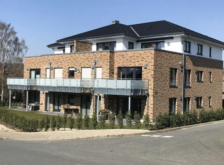 Middendorf-Bau GmbH: Mehrfamilienhaus mit Backsteinfassade, Balkonen und dunklem Dach an sonnigem Tag.