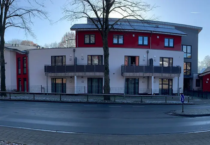 Ansicht eines modernen Gebäudes mit roten und weißen Fassaden, Balkonen und Bäumen im Vordergrund.