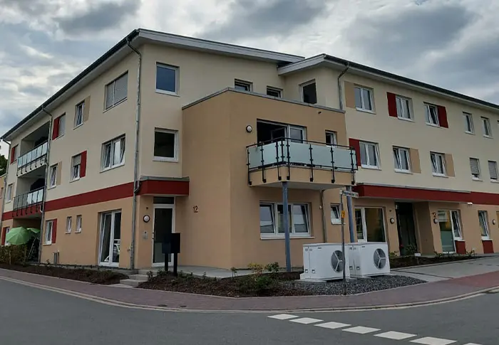 Ansicht eines modernen Mehrfamilienhauses mit Balkon, hellem Fassadenanstrich und klarem, zeitgemäßem Design.