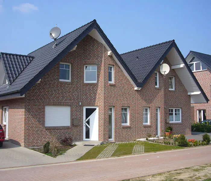 Ansicht eines neu gebauten Backsteinhauses mit Satteldach, inklusive Antenne und gepflastertem Gehweg.