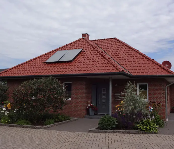Ansicht eines Einfamilienhauses mit roten Ziegeln, Solarpanelen und gepflegtem Vorgarten.