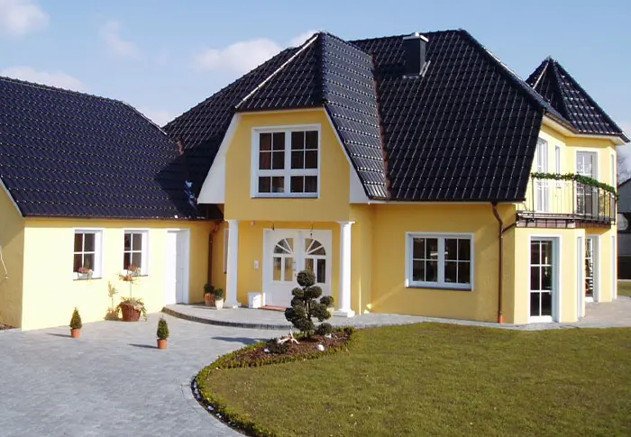 Gelbes Haus mit dunklem Dach und weißen Fensterrahmen, umgeben von gepflegtem Rasen.