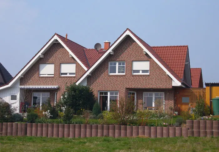 Referenz Hausbau: Rotklinkerhaus mit Giebeldach und gepflegtem Vorgarten.
