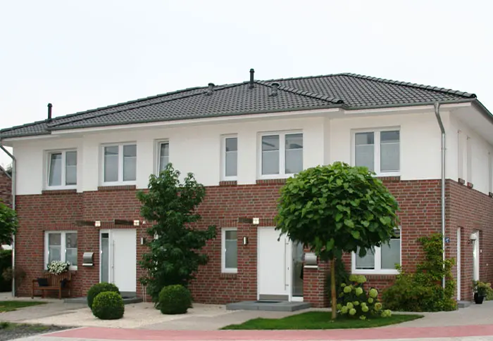 Referenz Hausbau: Fassade eines modernen Doppelhauses mit Klinker und weißen Elementen, graues Dach.