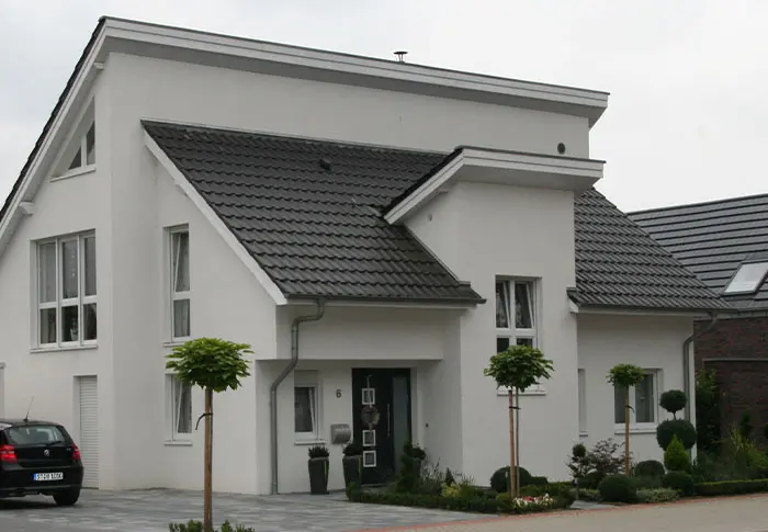 Referenz Hausbau: Modernes, weißes Einfamilienhaus mit dunklem Ziegeldach und gepflegtem Vorgarten.