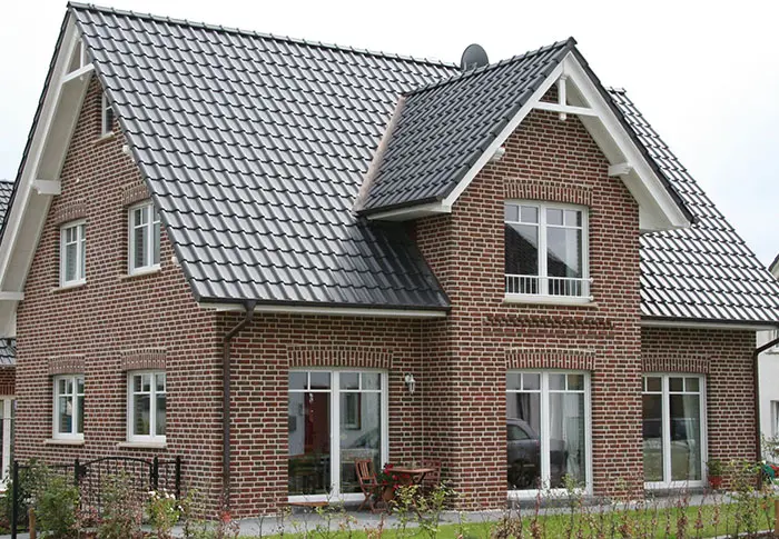 Referenz Hausbau: Detailansicht eines zweistöckigen Hauses mit roter Backsteinfassade und dunklem Ziegeldach.