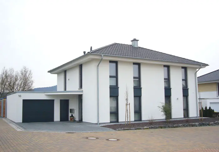 Referenz Hausbau: Modernes, weißes Haus mit Garage und dunklen Fensterrahmen. Neubau Einfamilienhaus.