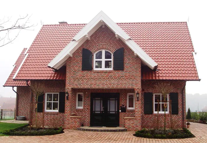 Referenz Hausbau: Fassade eines Einfamilienhauses mit rotem Ziegeldach und Backsteinen.