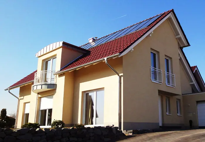 Referenz Hausbau: Ansicht eines modernen Einfamilienhauses mit rotem Ziegeldach und Solarpanelen.