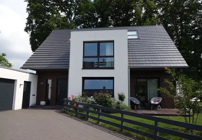 Referenz Hausbau: Modernes Einfamilienhaus mit grauen Dachziegeln, weißen Wänden und dunklen Fenstern.