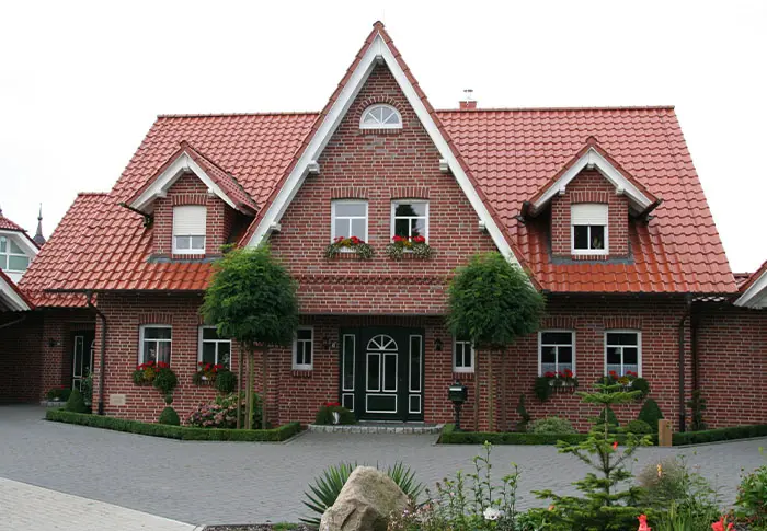 Referenz Hausbau: Fassade eines zweistöckigen Einfamilienhauses mit rotem Ziegeldach und gepflegtem Vorgarten.