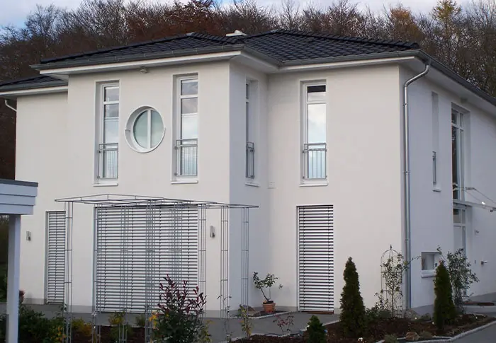 Ansicht eines modernen, weißen Hauses mit dunklem Dach und runden Fenster als Referenz Hausbau.