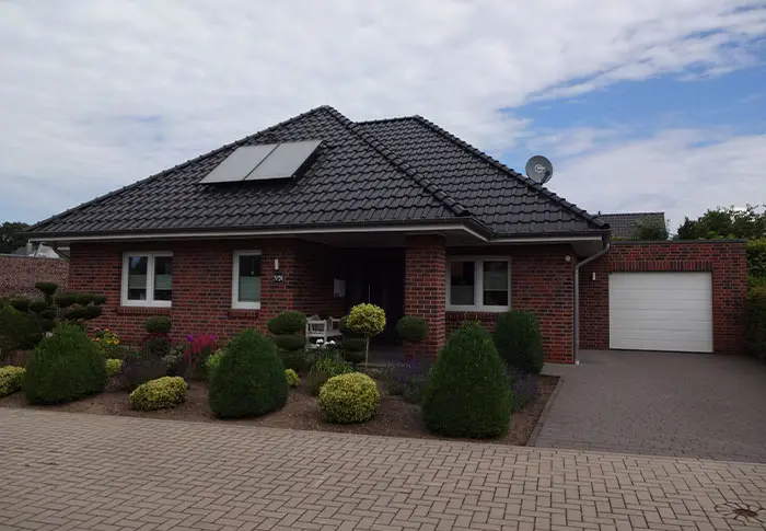 Referenz Hausbau: Ansicht eines modernen Einfamilienhauses mit roter Backsteinfassade, dunklem Ziegeldach und gepflegtem Vorgarten.