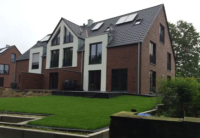 Referenz Hausbau: Fassade eines modernen Hauses mit Ziegeln, weißen Elementen und einem gepflegten Rasen.