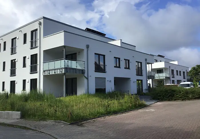 Neues, modernes Wohngebäude mit Balkonen und klaren Linien, umgeben von Grünflächen.