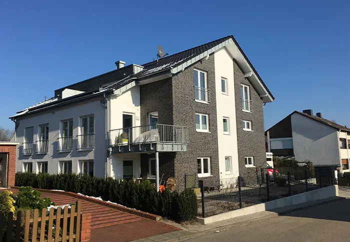 Referenz Wohnungsbau: Mehrfamilienhaus mit Balkonen und Fassade in Weiß und Grau. Neubau.