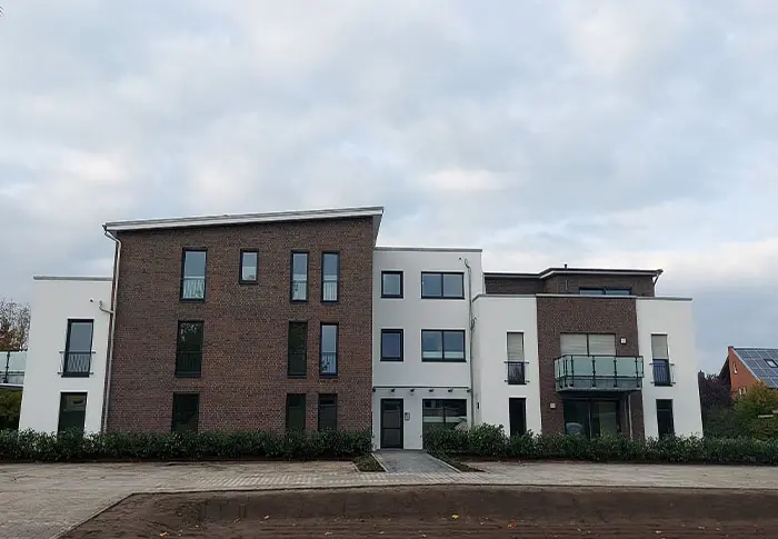 Referenz Wohnungsbau: Mehrfamilienhaus mit Fassade aus Backstein und weißem Putz.