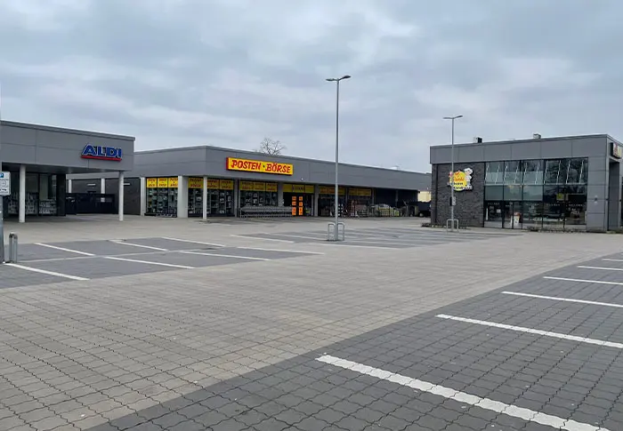 Gewerbebau: Ansicht von Aldi, Posten Börse und Bäckerei mit Parkplätzen vor den Gebäuden.