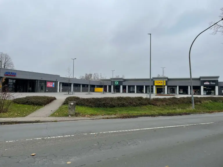 Foto eines Einkaufszentrums mit Geschäften wie Aldi, Deichmann und Takko bei Tageslicht.
