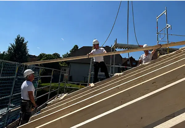 Handwerker mit Schutzhelmen montieren Holzbalken auf einem Dachstuhl bei der Middendorf Bau GmbH