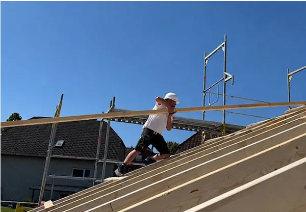 Handwerker mit Schutzhelm montiert Holzbalken auf einem Dachstuhl bei der Middendorf Bau GmbH