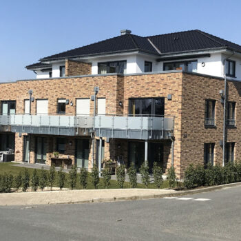 Middendorf-Bau GmbH: Mehrfamilienhaus mit Backsteinfassade, Balkonen und dunklem Dach an sonnigem Tag.