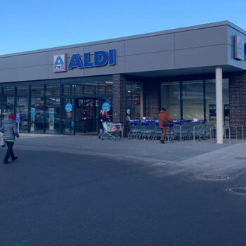 Außenansicht eines ALDI-Marktes mit Kunden und Einkaufswagen vor dem Eingang.
