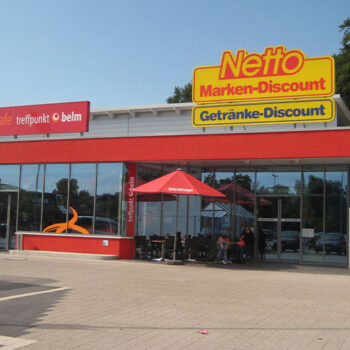 Außenansicht eines Netto Marken-Discount und Brinkhege Cafe Treffpunkt mit roter Markise und Kunden.