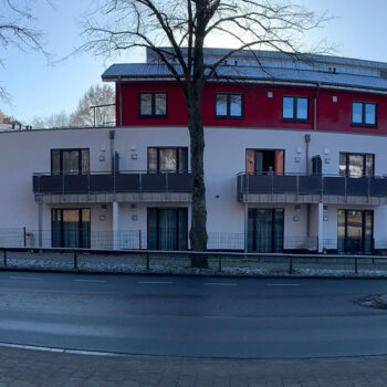 Ansicht eines modernen Gebäudes mit roten und weißen Fassaden, Balkonen und Bäumen im Vordergrund.