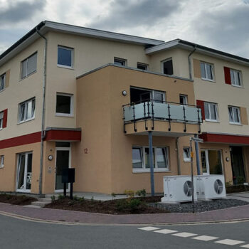 Ansicht eines modernen Mehrfamilienhauses mit Balkon, hellem Fassadenanstrich und klarem, zeitgemäßem Design.
