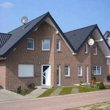 Ansicht eines neu gebauten Backsteinhauses mit Satteldach, inklusive Antenne und gepflastertem Gehweg.