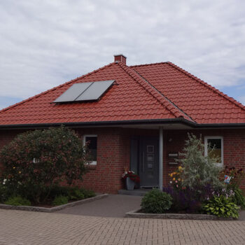 Ansicht eines Einfamilienhauses mit roten Ziegeln, Solarpanelen und gepflegtem Vorgarten.