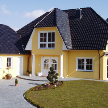 Gelbes Haus mit dunklem Dach und weißen Fensterrahmen, umgeben von gepflegtem Rasen.