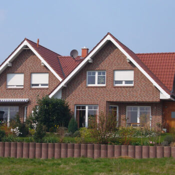 Referenz Hausbau: Rotklinkerhaus mit Giebeldach und gepflegtem Vorgarten.