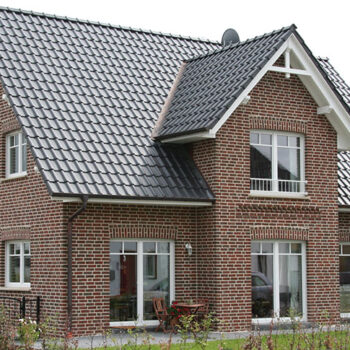 Referenz Hausbau: Detailansicht eines zweistöckigen Hauses mit roter Backsteinfassade und dunklem Ziegeldach.
