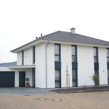 Referenz Hausbau: Modernes, weißes Haus mit Garage und dunklen Fensterrahmen. Neubau Einfamilienhaus.
