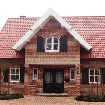 Referenz Hausbau: Fassade eines Einfamilienhauses mit rotem Ziegeldach und Backsteinen.