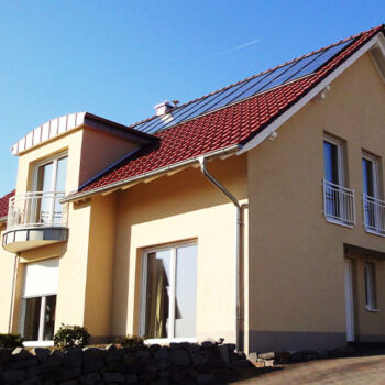 Referenz Hausbau: Ansicht eines modernen Einfamilienhauses mit rotem Ziegeldach und Solarpanelen.