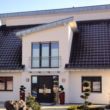 Referenz Hausbau: Modernes, zweistöckiges Haus mit dunklem Ziegeldach und hellem Fassadenputz