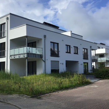 Neues, modernes Wohngebäude mit Balkonen und klaren Linien, umgeben von Grünflächen.