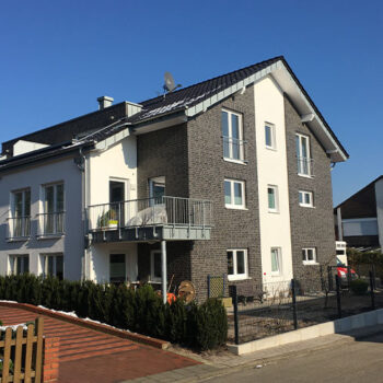 Referenz Wohnungsbau: Mehrfamilienhaus mit Balkonen und Fassade in Weiß und Grau. Neubau.