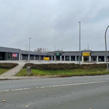Foto eines Einkaufszentrums mit Geschäften wie Aldi, Deichmann und Takko bei Tageslicht.